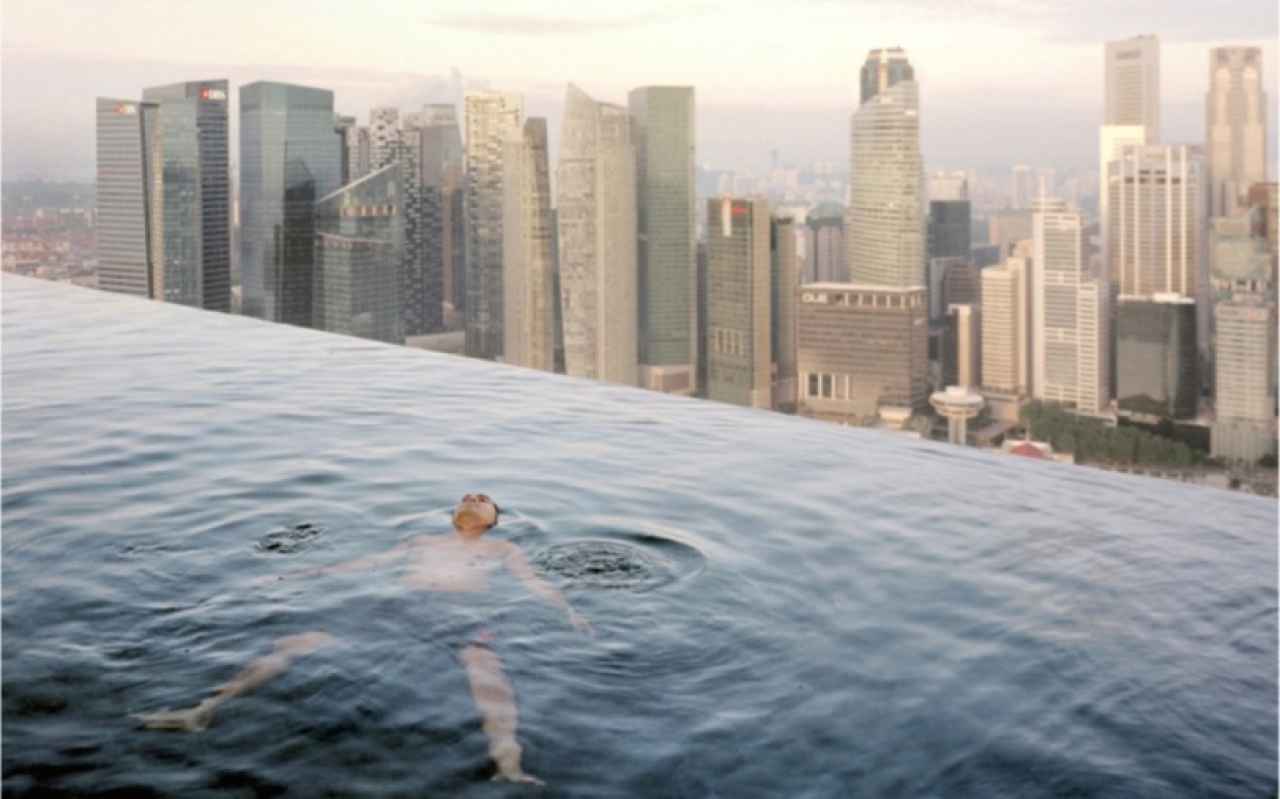 A man floats in the 57th-floor swimming pool of the Marina Bay Sands Hotel, with the skyline of the Singapore financial district behind him. 2013 © Paolo Woods & Gabriele Galimberti--INSTITUTE